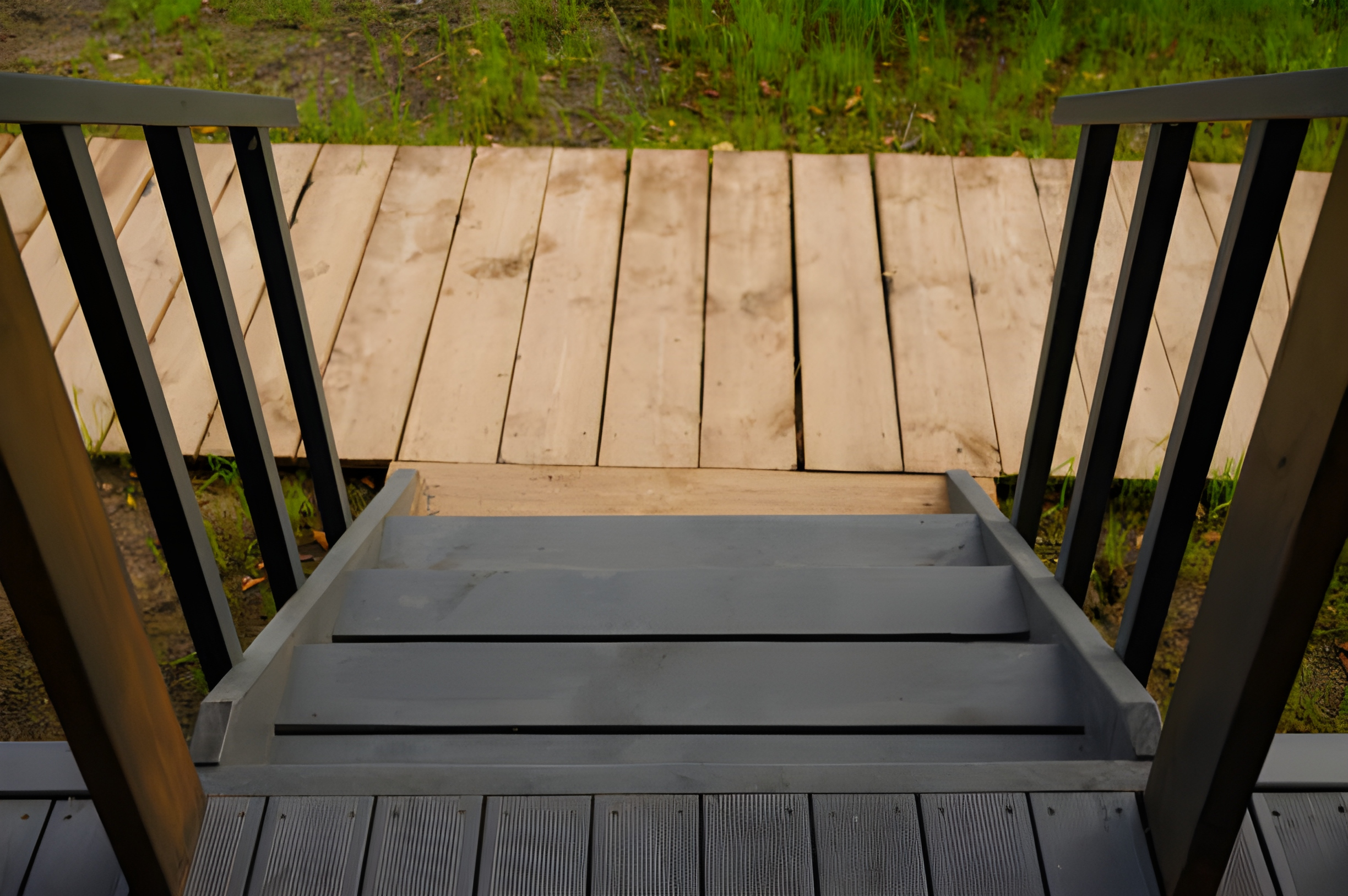 View of a black stairs with trim on the side, leading down to a wooden platform. Vertical shot